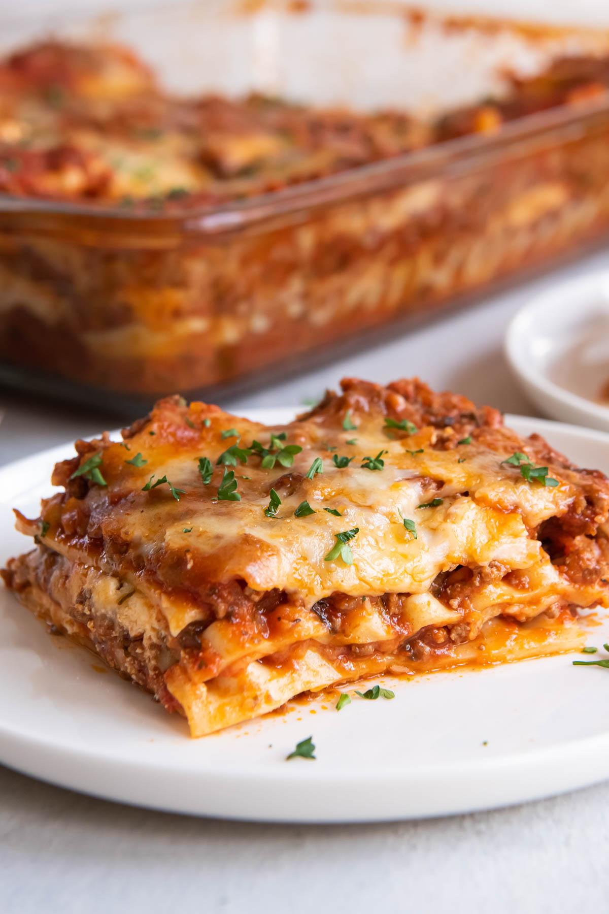 How to make the BEST homemade lasagna! This classic lasagna recipe is cheesy, saucy and full of flavor! Make this easy lasagna recipe with ricotta for a family dinner or to feed a crowd. Slice of lasagna on a small plate.